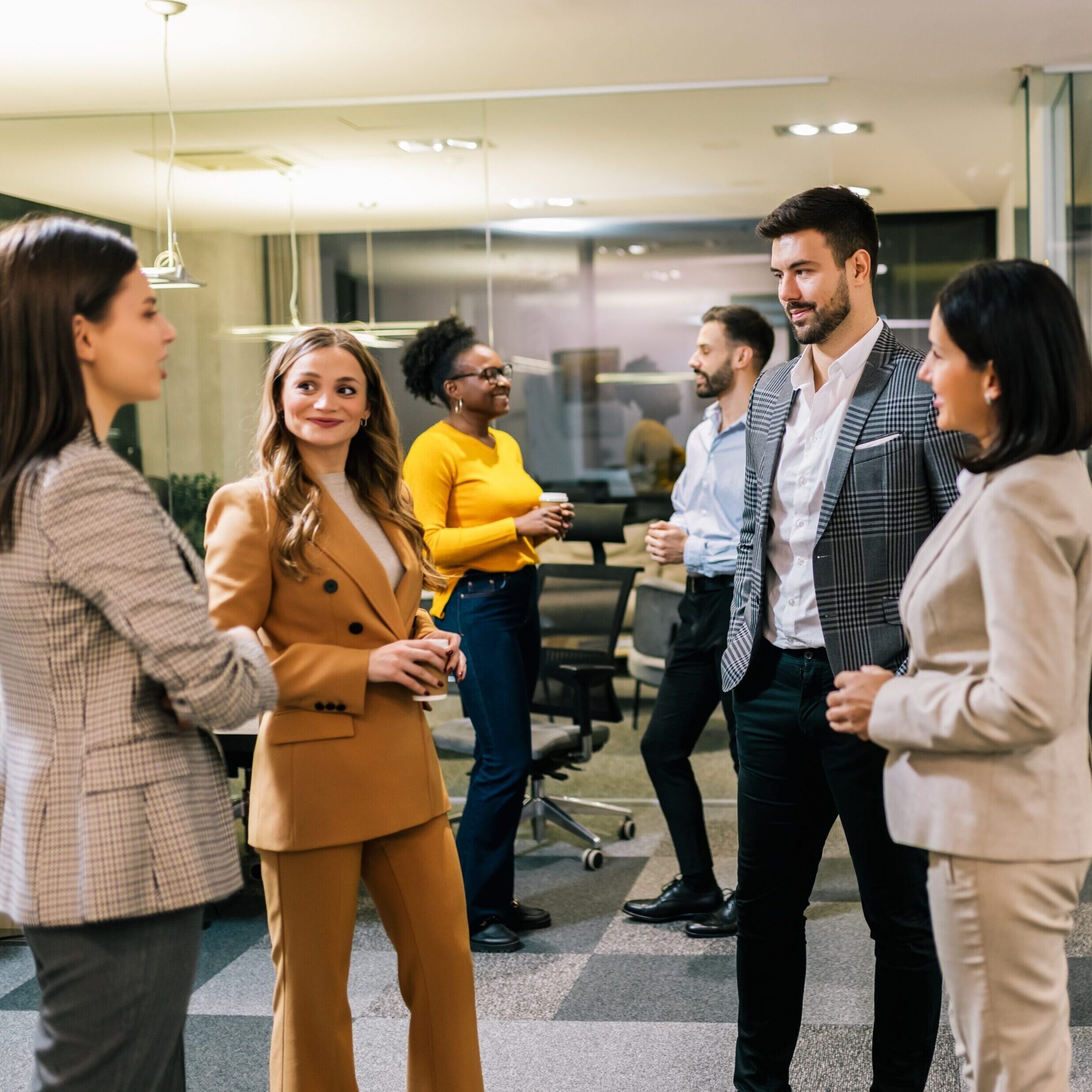 Three professionals smile during conversation over coffee.