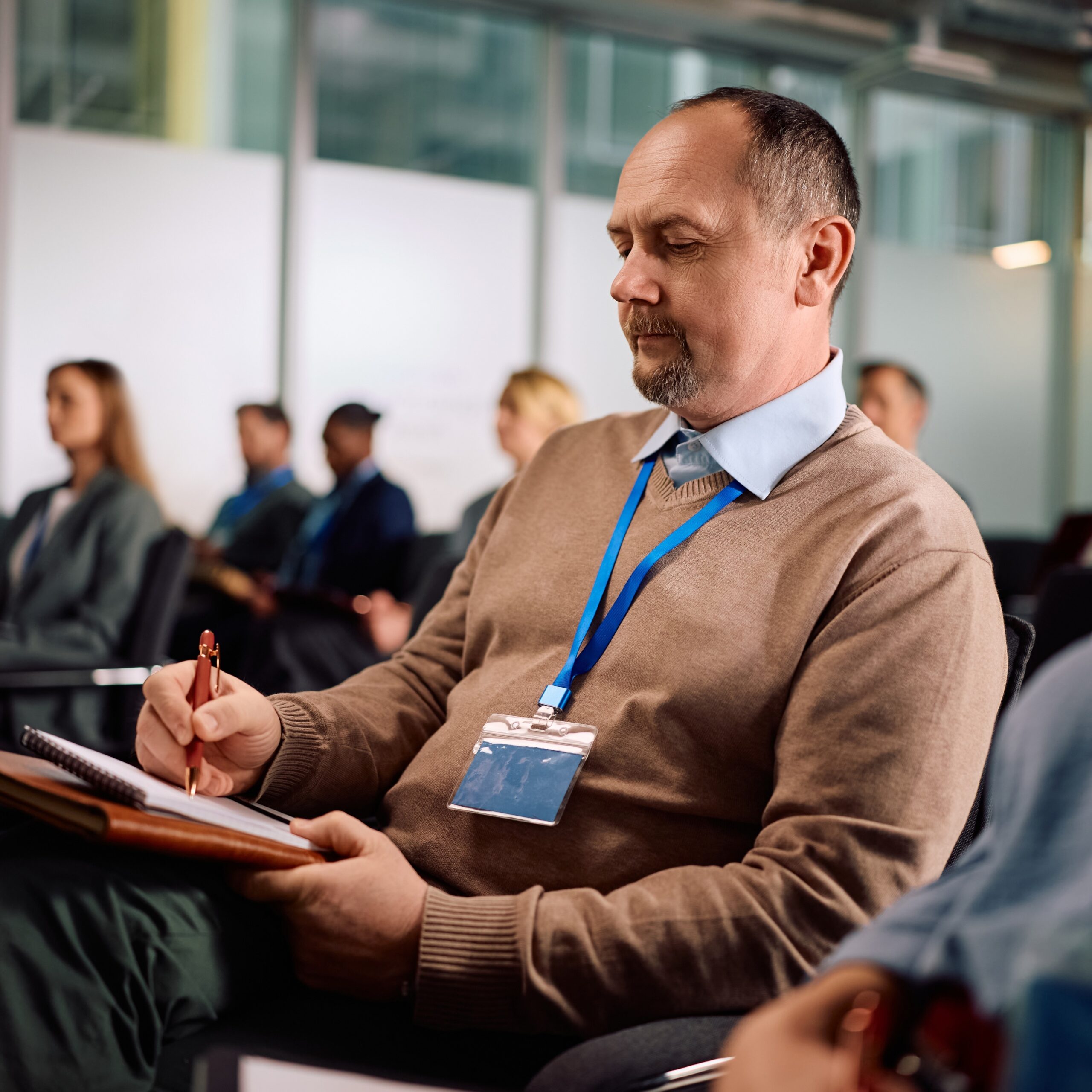 A man sitting in an audience of a conference takes notes.